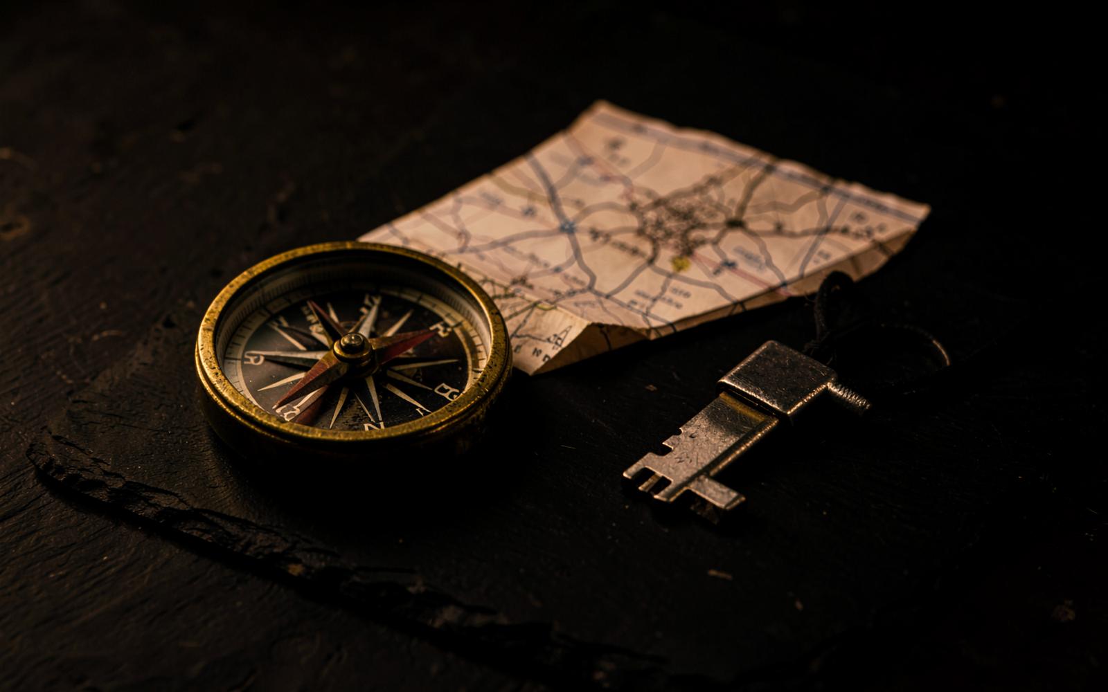 A brass compass, a paper map and a small metal key on a dark slate surface